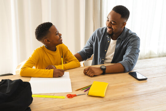 Father and son bonding while doing homework at home, smiling and engaged