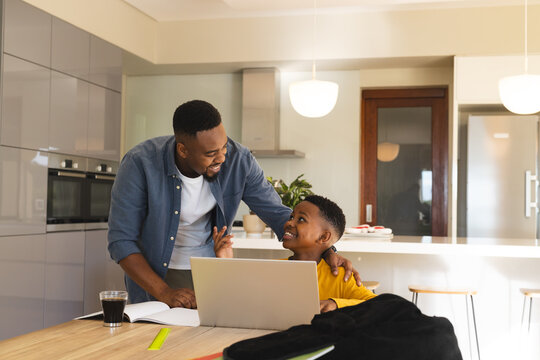 Father helping son with homework at kitchen table, both smiling and engaged