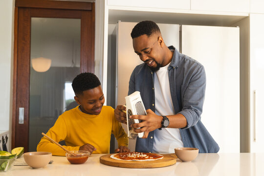 Father and son making pizza together in kitchen, smiling and enjoying time