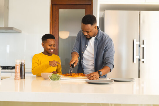 Father and son enjoying pizza together in modern kitchen, sharing happy moments