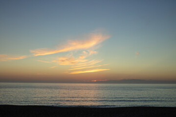 Obraz premium A calm sunset over Melides Beach on Portugal’s Alentejo coast, where soft golden hues and gentle clouds reflect on the still Atlantic waters, creating a peaceful and serene seascape.