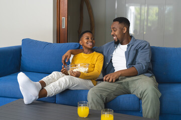 Father and son enjoying popcorn and bonding on cozy blue sofa at home