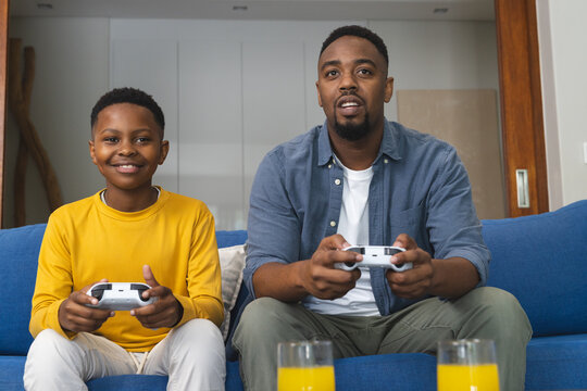 African American father and son playing video games together on couch at home