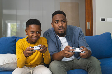 African American father and son playing video games on couch, enjoying time together