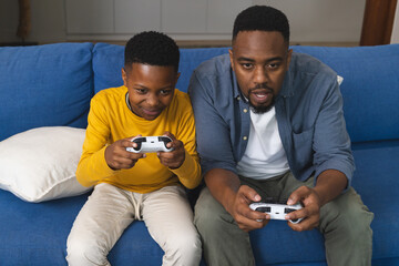Father and son playing video games on couch, enjoying quality time together