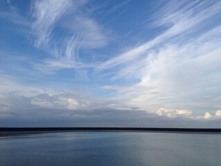 Obraz premium Sky with streaked cirrus clouds and calm water. Minimalist nature scene perfect for backgrounds, environmental themes, or designs emphasizing peace and clarity.