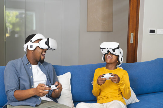 African American father and son playing video games with VR headsets at home