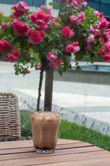 Mocha coffee in a glass on a café patio table by a rose bush