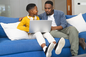 Father and son using laptop on couch, bonding and learning together at home