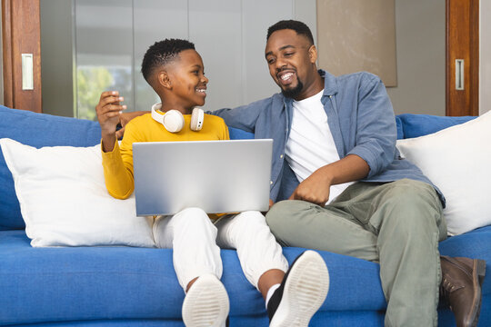 Father and son bonding on couch, using laptop and enjoying quality time