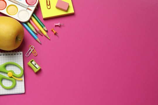 Various educational supplies including pencils, notebooks, green apple and stationery placed on colorful surface, top view