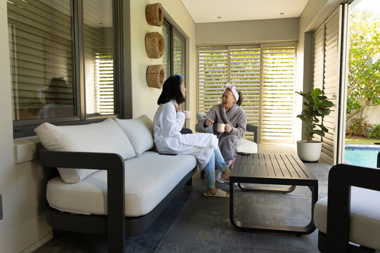 Asian adult mother and daughter sitting on modern sofa in indoor lounge, sharing gentle conversation