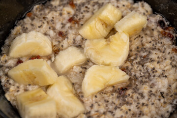 ripe banana in quickly cooked oatmeal porridge, boiled oatmeal porridge with chia seeds, berries and fresh banana, close up, side view
