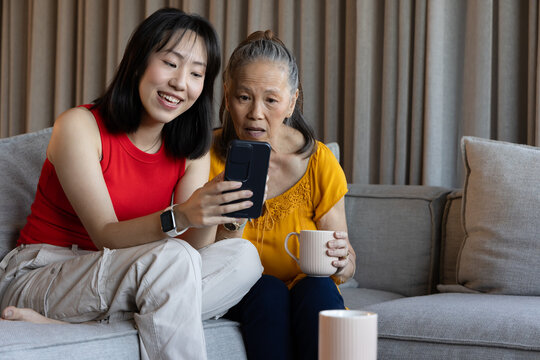 Young woman showing smartphone to older woman on sofa, both smiling and engaged