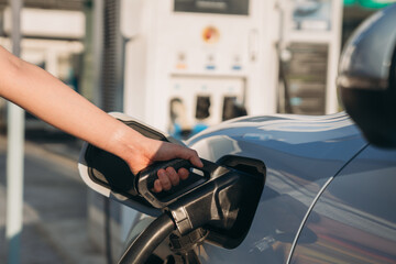Close-up of a hand plugging an electric vehicle charger into a charging station, clean energy and...