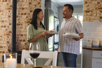 Asian woman and man enjoying conversation while setting table at home