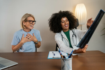 Confident beautiful female doctor and mature woman patient looking at x-ray or MRI concept...
