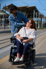 Obraz premium Man assisting woman in wheelchair at tram or train station - wheelchair and disability concept