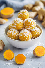 Anti-Inflammatory Golden turmeric and ginger energy bites stacked in a small white bowl, dusted with shredded coconut.