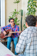 Fototapeta premium Young man playing acoustic guitar for friends at home gathering