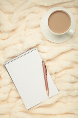 Cup of coffee and notebook on bed with soft beige plaid. Copy space. Vertical photo