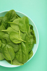 Baby spinach leaves with water drops in mint bowl on mint background. Vertical photo