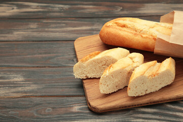 Baguette whole and cut into pieces on cutting board on brown background