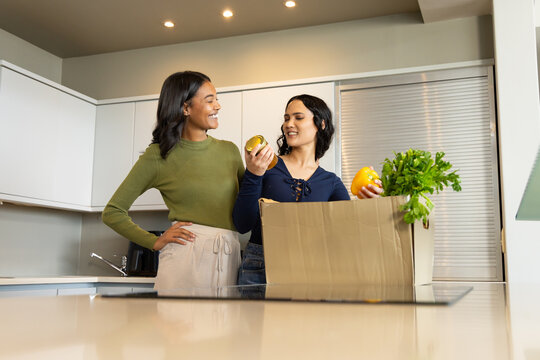 Diverse female friends unpacking groceries in modern home kitchen, with bell peppers and glass jar