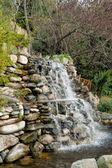 Stone waterfall cascades through lush plants in a peaceful garden
