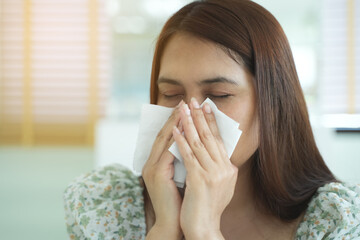 A young woman sneezing into a tissue, showing symptoms of a cold or allergy. Healthcare, illness,...