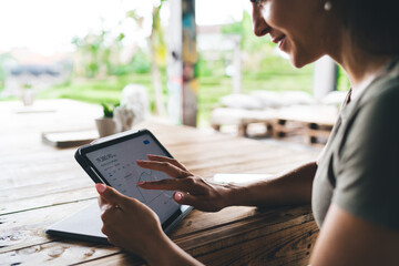 Smiling woman reviewing cryptocurrency graph on tablet in tropical setting, working remotely with focus on investment growth and digital finance in a serene natural workspace