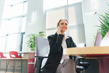 Professional woman engaged in a cheerful phone conversation in a modern office space during the daytime