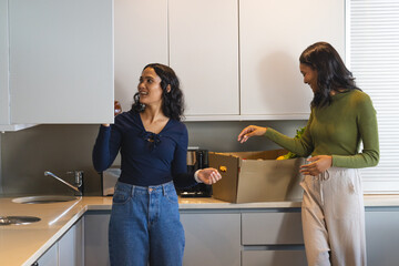 Unpacking Diverse female friends grabbing jar while sorting produce at kitchen counter, with sink