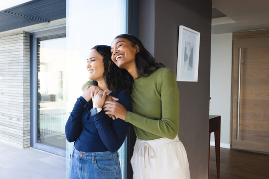 Leaning two women hugging inside modern home by sliding glass door, with smartwatch detail - Powered by Adobe