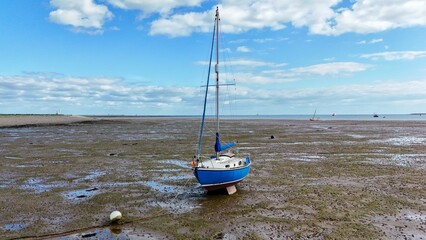 Blue-hulled boat beached on coastal flats during low tide under a spring sky