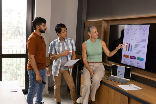 Presenting diverse coworkers pointing at charts in modern conference room, with laptop and reports