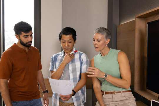 Diverse coworkers reviewing printed report charts in office lounge, with red pen and smartwatch