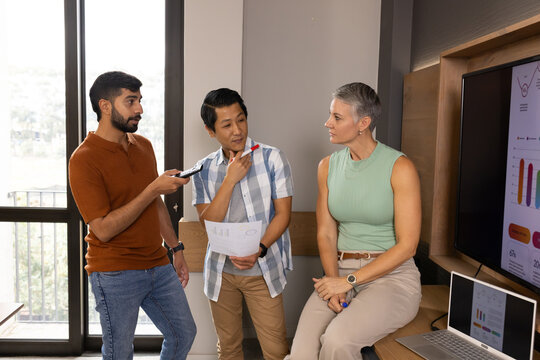 Analyzing charts Diverse coworkers working in office nook, with remote, laptop and monitor