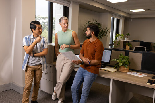Diverse coworkers discussing chart data with pen at open-plan office desk, with computers