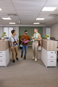 Walking Diverse coworkers holding smartphone and notebook in office corridor, with potted plants
