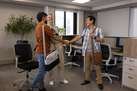 Shaking hands Diverse coworkers greeting in open-plan office, with messenger bags and monitors - Powered by Adobe
