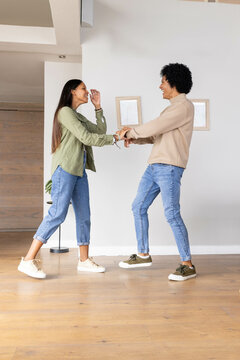 Dancing diverse couple gliding on hardwood floor in living room, with plant and frames, copy space
