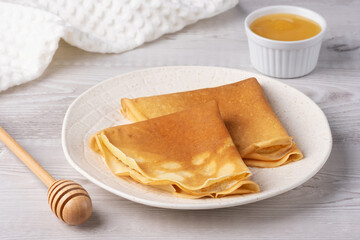 Traditional Russian pancakes with honey on a white wooden table