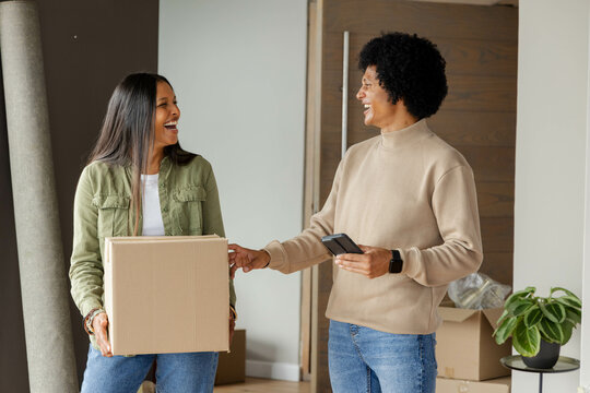 Diverse couple unpacking boxes and discussing paint colors in new home entry, with paint swatch fan