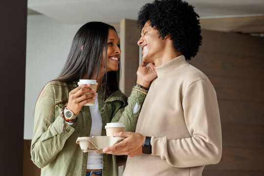 Touching partner's face, diverse couple holding coffee cups at modern lobby, with drink carrier