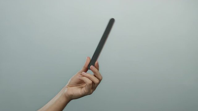 Caucasian male hand holding an emery board against a plain white background, highlighting simplicity and grooming.