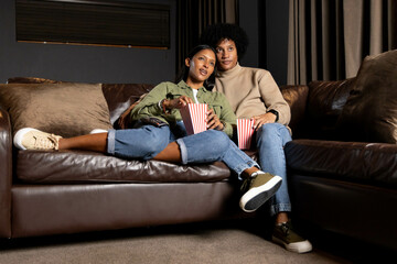 Watching Diverse couple sitting on leather sofa in living room, holding striped popcorn containers