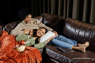 Relaxing diverse couple lounging on leather sofa in living room, with popcorn and throw blanket