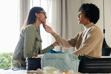 Smiling man and Indian woman exchanging touch while packing items at home, with open black suitcase