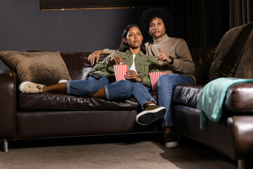 Eating popcorn from striped containers Diverse couple sitting in home theater, with TV remote